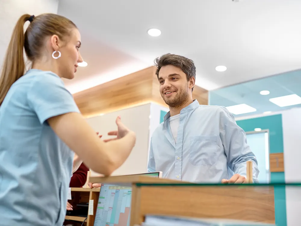 Paciente conversando con una recepcionista de clínica dental en el mostrador